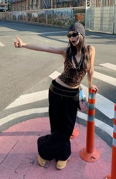 Woman in a leopard print top and black pants on a street, giving a thumbs up