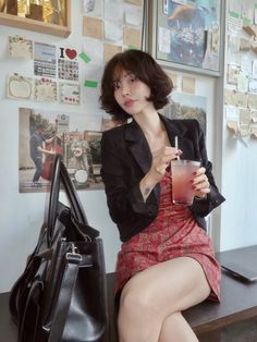 Woman with short hair in a red dress and black blazer holding a drink