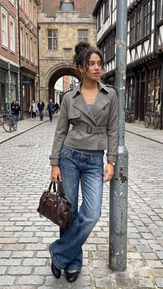 Woman with curly hair in an updo wearing a trench coat and jeans on a cobblestone street