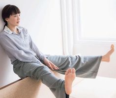 Woman in pajamas sitting indoors with bare feet, looking out a window