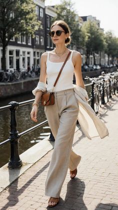 Woman in a white tank top and wide leg pants walking along a canal
