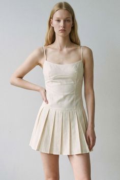 Woman with blonde hair wearing a light-colored pleated dress indoors