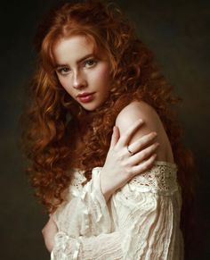 Woman with red curly hair and freckles wearing a white off-shoulder dress