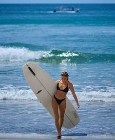 Woman in a black bikini holding a surfboard on a beach
