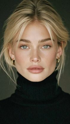 Woman with blonde hair and blue eyes wearing a black turtleneck and gold earrings