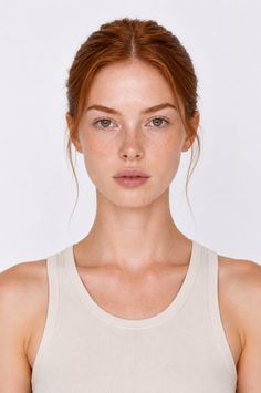Woman with red hair and freckles wearing a tank top against a white background