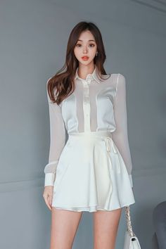 Woman in a white sheer shirt and mini skirt against a gray background