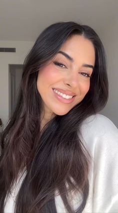 Woman with long dark hair smiling in a white top indoors