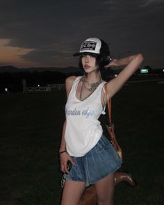 Woman in a baseball cap and denim skirt posing outdoors at night