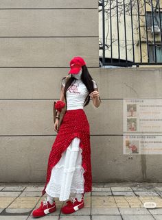 Woman in a red skirt and white top with a red cap standing on a street