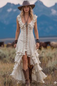 Woman in a ruffled dress, cowboy hat, and boots in a field with mountains