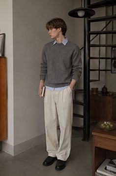 Man in a gray sweater and light pants standing indoors