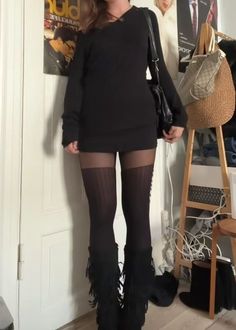 Woman in a black dress, black tights, and fringe boots standing indoors
