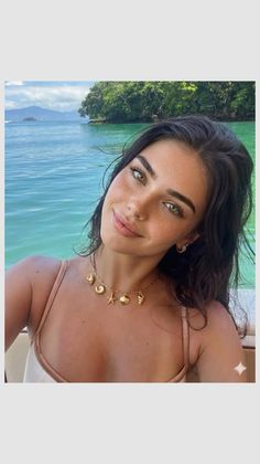 Woman with long dark hair and freckles wearing a bikini and shell necklace on a tropical island