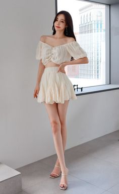 Woman in an off-shoulder top and mini skirt posing indoors by a window