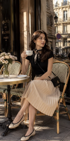 Woman in a black top and pleated skirt sitting at an outdoor cafe in Paris