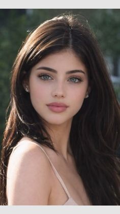 Woman with long dark hair and blue eyes wearing a light-colored top outdoors