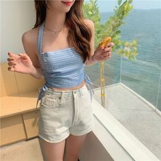 Woman in a blue gingham top and denim shorts by the ocean