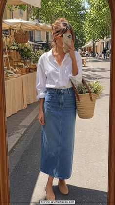 Woman in a denim skirt and white shirt taking a mirror selfie at a street market