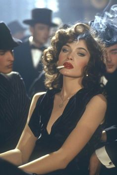 Woman with curly hair and red lipstick smoking in a dark, crowded room