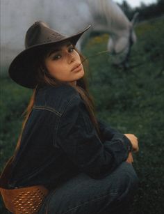 Woman in a cowboy hat and denim jacket with a horse in the background