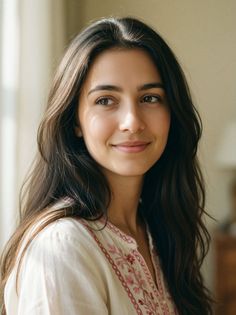 Woman with long dark hair wearing an embroidered white shirt indoors