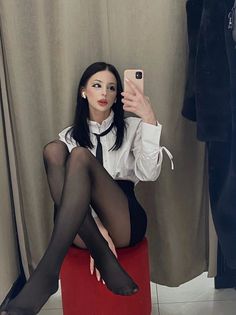 Woman in a white shirt and black tie taking a mirror selfie while sitting