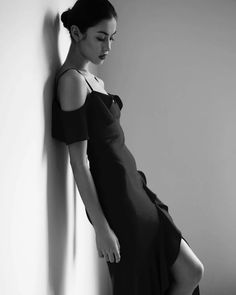Woman in a black dress with a high slit leaning against a wall