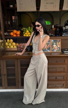 Woman in a vest and wide leg pants talking on the phone at a fruit stand