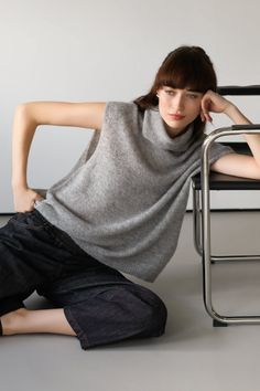 Woman in a gray sweater and dark jeans sitting on the floor in a studio