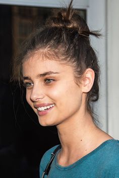 Woman with a messy bun and green eyes smiling, captured in a close-up portrait