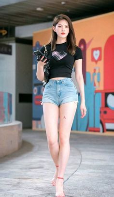 Woman in a black crop top and denim shorts walking barefoot outdoors