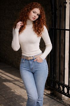 Woman with curly red hair wearing a white turtleneck and jeans outdoors