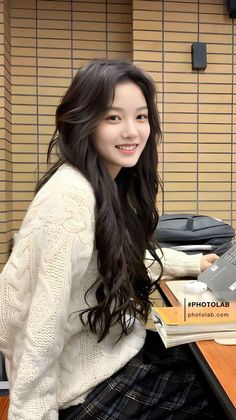 Young woman with long dark hair smiling in a white sweater and plaid skirt