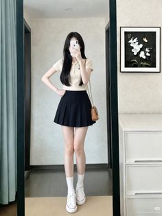 Woman in a polo shirt and pleated skirt taking a mirror selfie indoors