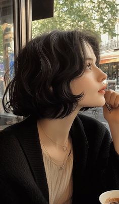 Woman with short wavy black hair wearing a black cardigan and layered necklaces indoors
