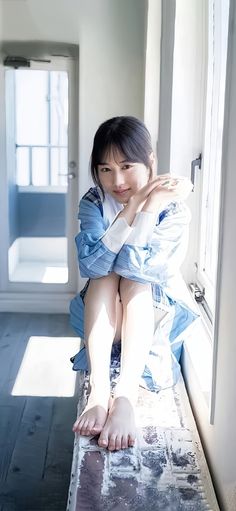 Woman in a blue dress sitting by a window with bare feet