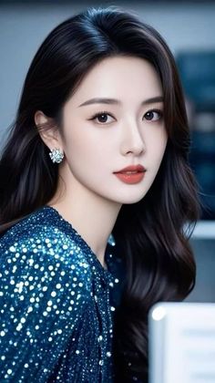 Woman with long black hair wearing a blue sequin dress and earrings
