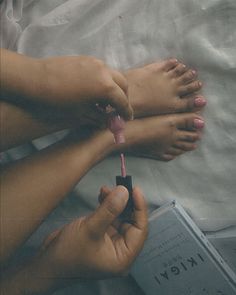 Person painting their toenails pink while holding a book