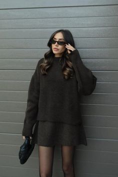 Woman in a dark sweater and mini skirt with sunglasses and a black handbag
