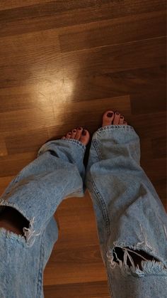 Person wearing ripped light wash jeans with bare feet on a wooden floor