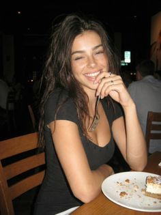 Woman with long hair and freckles smiling and winking in a dark indoor setting