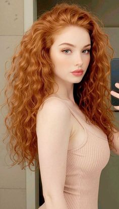 Woman with long red curly hair and blue eyes wearing a light pink top