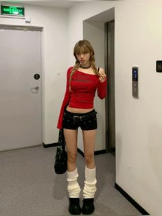 Woman with pigtails in a red top and black shorts with leg warmers indoors