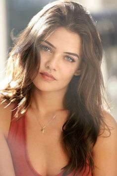 Woman with long brown hair and green eyes wearing a red top and cross necklace