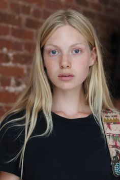 Young woman with blonde hair and blue eyes in a black t-shirt against a brick wall