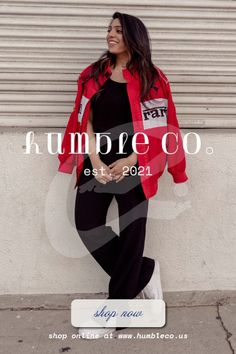 Woman in a red jacket and black outfit leaning against a wall outdoors
