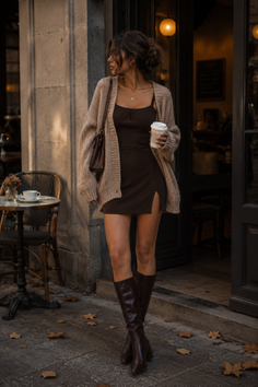 Woman in a brown dress and knee-high boots holding a coffee cup on a street