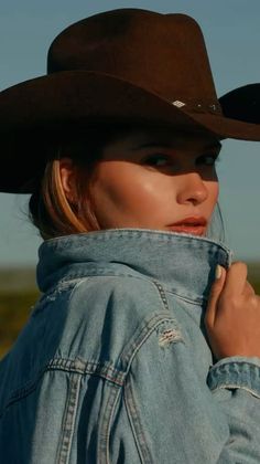 Woman in a cowboy hat and denim jacket looking over her shoulder outdoors