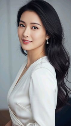 Woman with long dark hair wearing a white top and pearl earrings